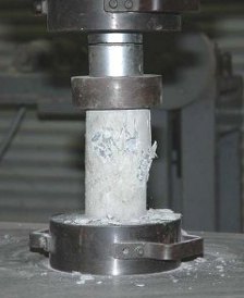 Concrete cylinder undergoing compression test at failure point